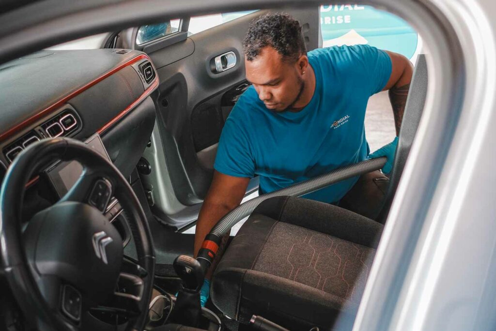 Un expert du vitrage nettoie l'intérieur du véhicule client chez Mondial Pare-Brise Réunion